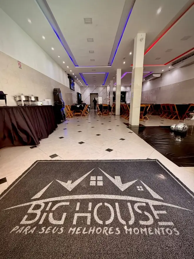 Salão amplo do Espaço Big House com tapete da marca, globo espelhado e mesa de buffet