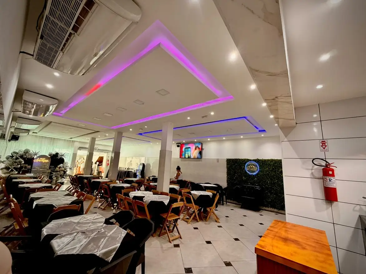 Salão do Espaço Big House com iluminação de LED roxa no forro, mesas postas e cadeiras de madeira
